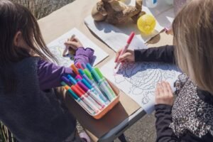 Two young girls coloring at a table with markers and crayons