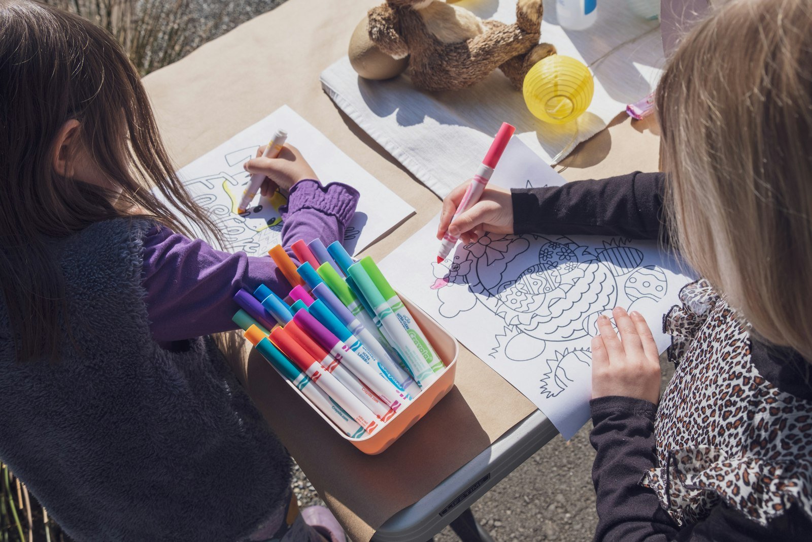 Two young girls coloring at a table with markers and crayons