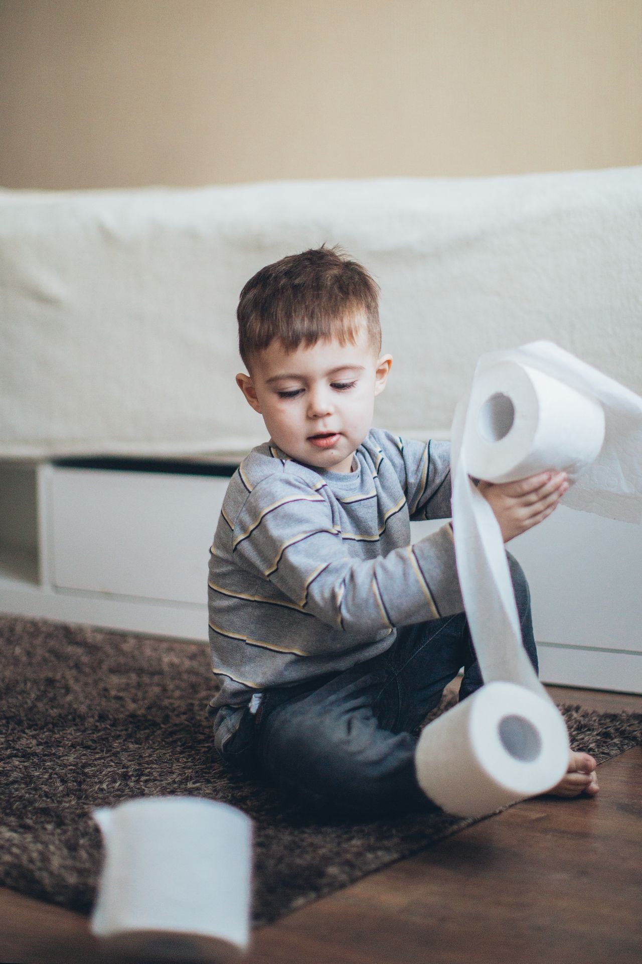 Toddler sitting on the floor playfully unrolling toilet paper